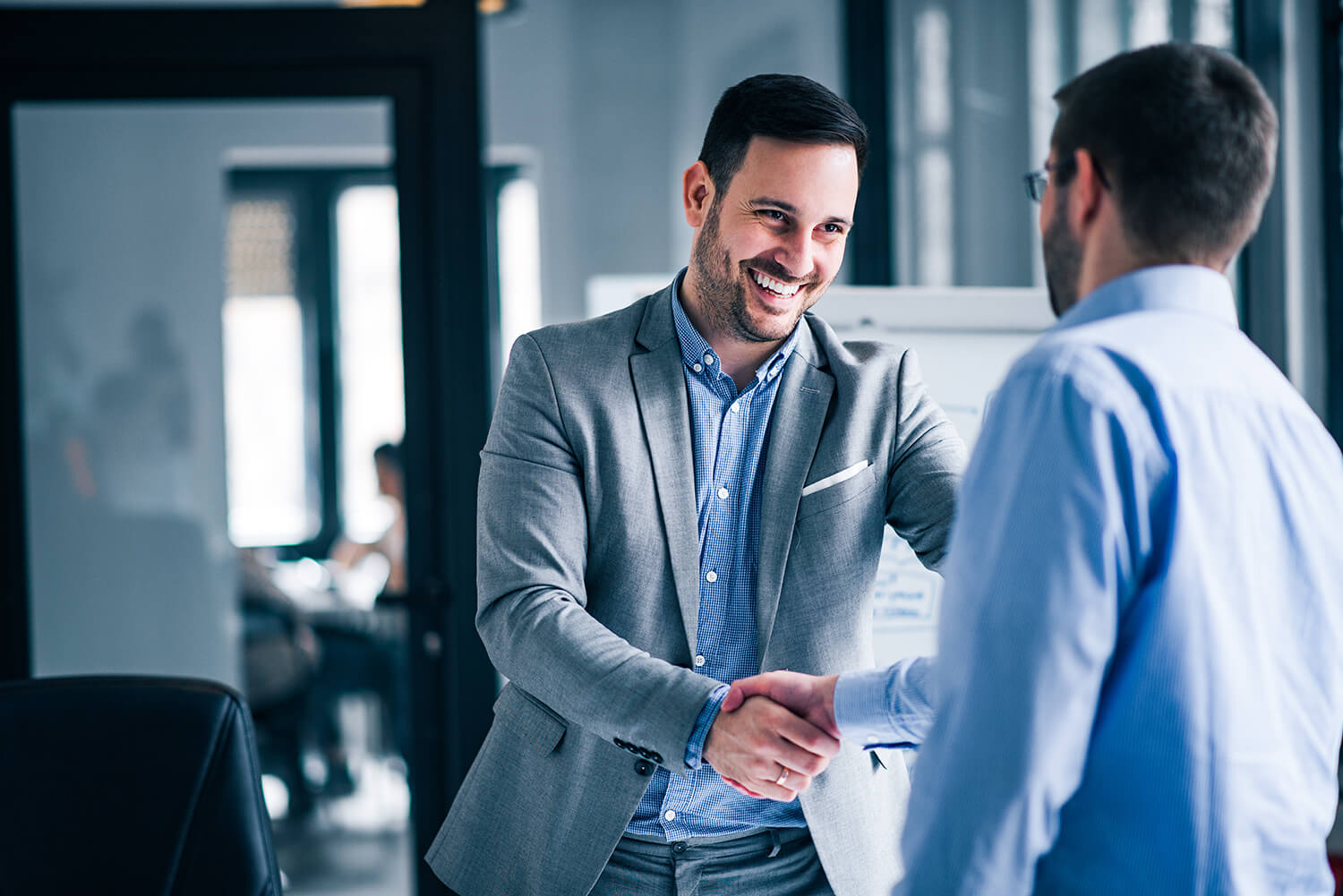two-smiling-businessmen-shaking-hands-while-standing-office